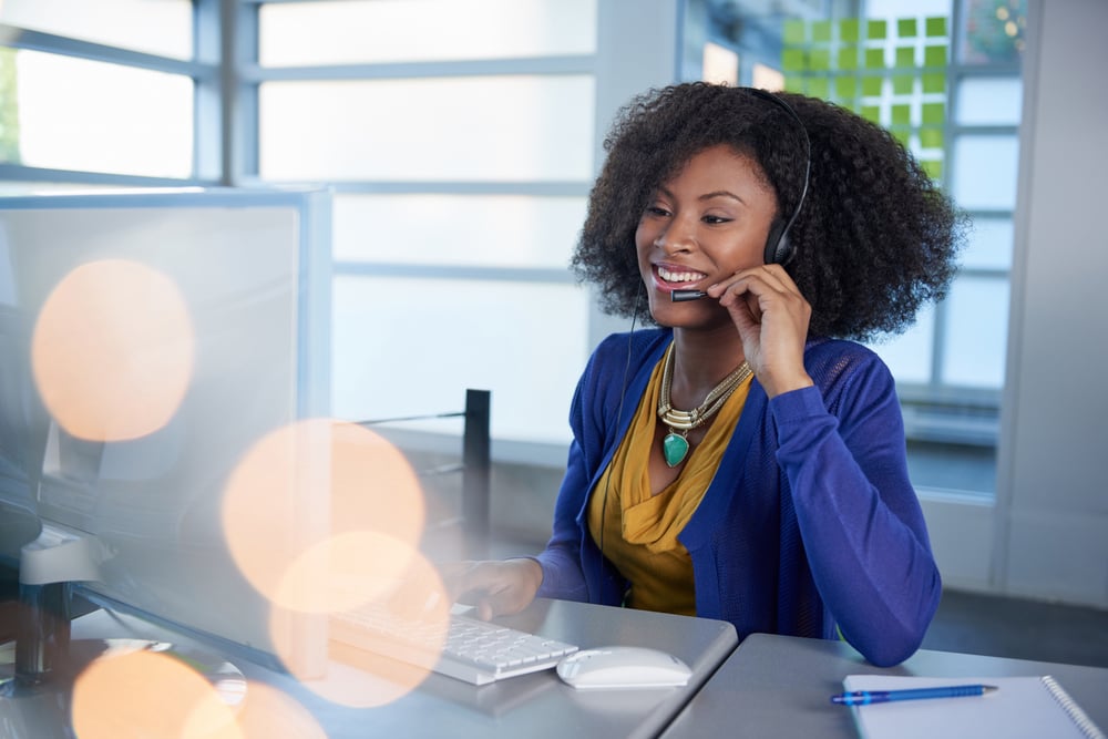 Portrait of a smiling customer service representative with an afro at the computer using headset Portrait of a smiling customer service representative with an afro at the computer using headset